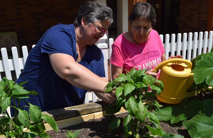 A caretaker and Memory Care resident tend to the garden